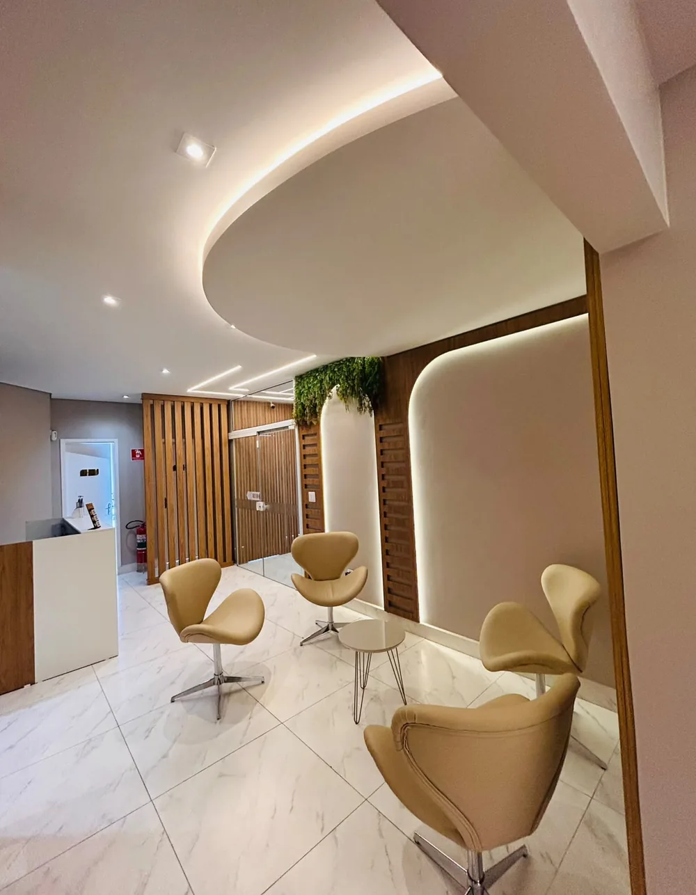 Sala de espera do Espaço Naka, com iluminação em sanca, plantas e poltronas confortáveis.
